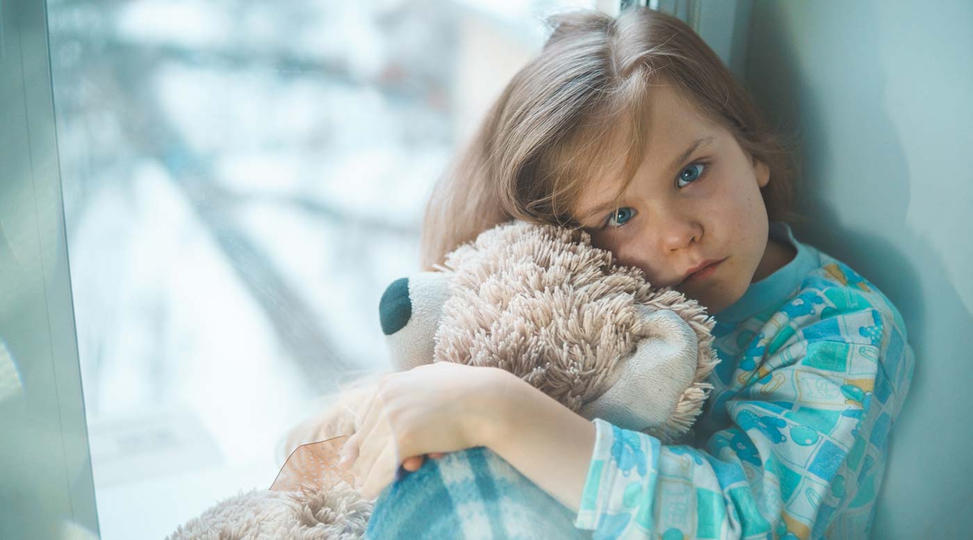 Bild på flicka som sitter på sin säng med en teddybjörn